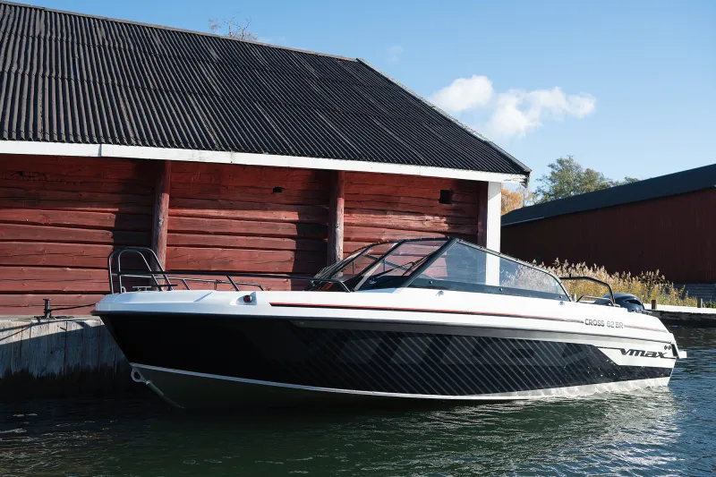 Cross 62 VMAX ligger förtöjd vid en brygga framför en röd lada vid vattnet, med sportig VMAX-design