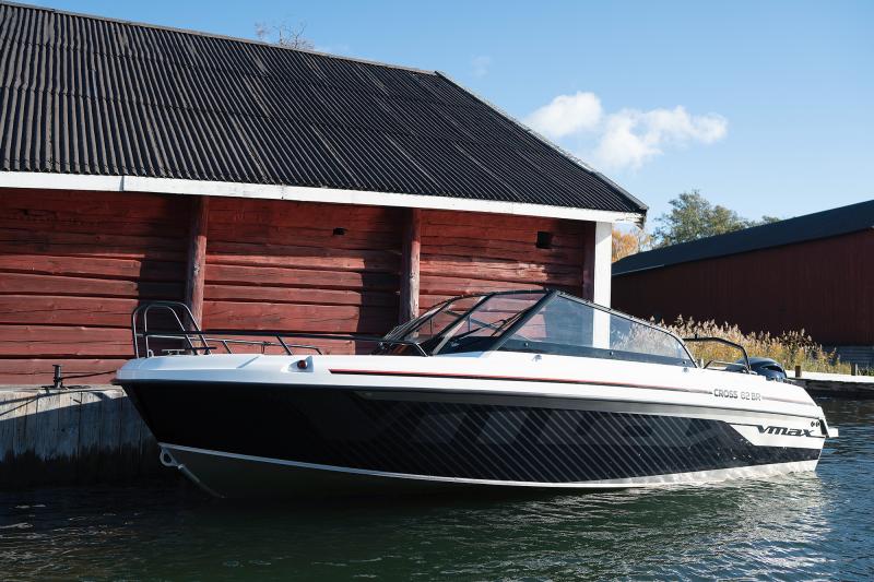 Cross 62 VMAX ligger förtöjd vid en brygga framför en röd lada vid vattnet, med sportig VMAX-design