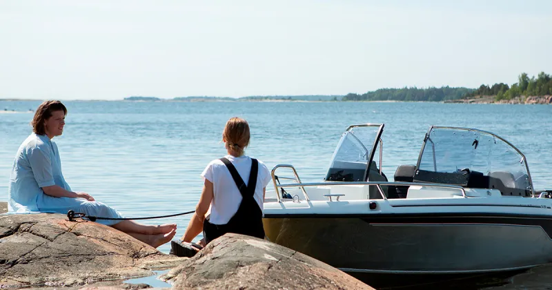 Kaksi henkilöä istuu rantakalliolla ja Cross 54 BR on kiinnitettynä rantaan.