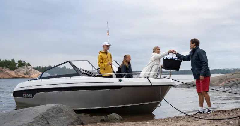 Cross 62 BR juuri rantautuneena hiekkarantaan. Kyydissä on kaksi lasta ja nainen, joka ojentaa eväskoria rannalla seisovalle miehelle.