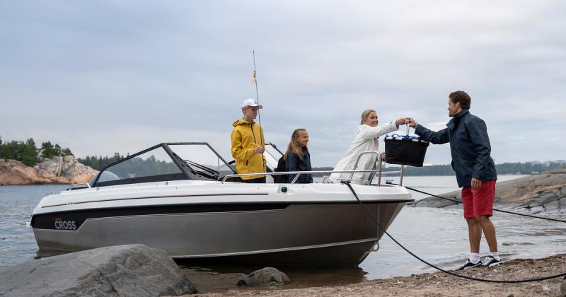 Cross 62 BR juuri rantautuneena hiekkarantaan. Kyydissä on kaksi lasta ja nainen, joka ojentaa eväskoria rannalla seisovalle miehelle.